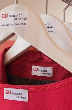 Kleiderbügel mit roten Kleidungsstücken, auf deren Etiketten ein dickes rotes GD prangt